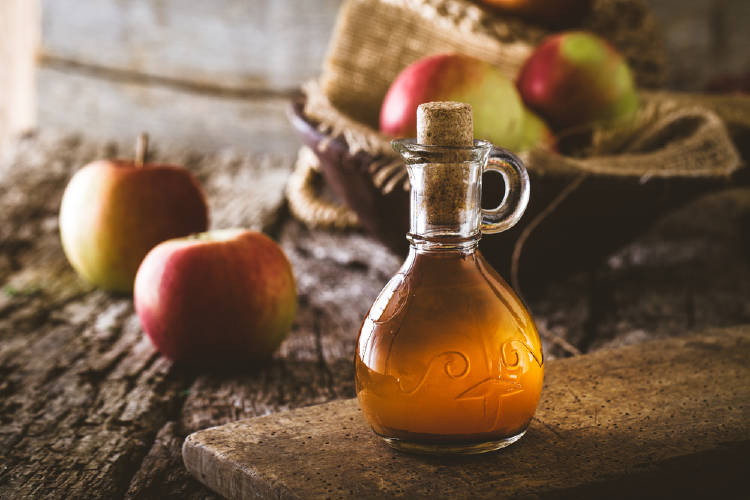 Una botella de vinagre con manzanas de fondo