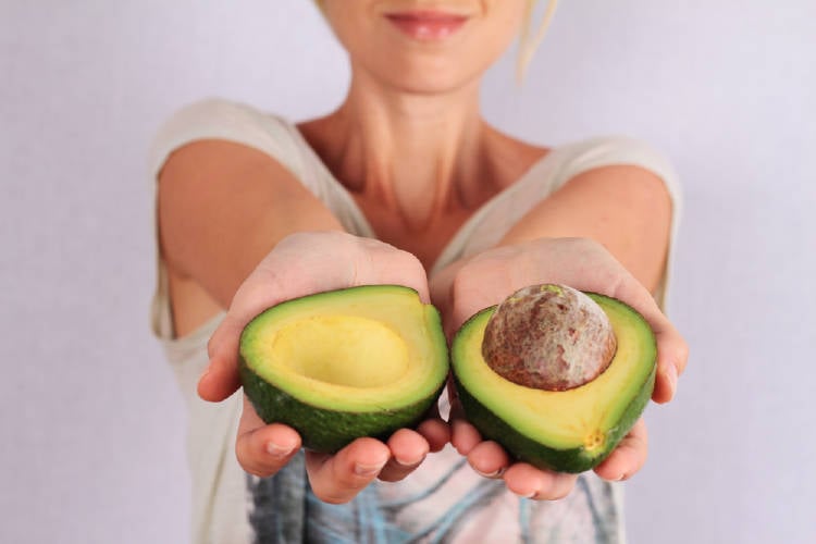 aguacate Una mujer muestra las dos mitades de un aguacate