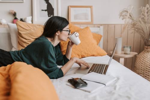 woman using laptop and drinking beverage in bed 4050415