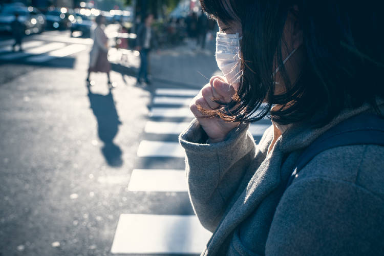 Una mujer con barbijo tose en la calle