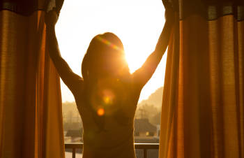 Una mujer abre las cortinas para dejar entrar la  luz del sol