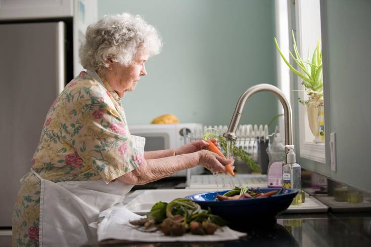 Mujer mayor en la cocina lavando verduras