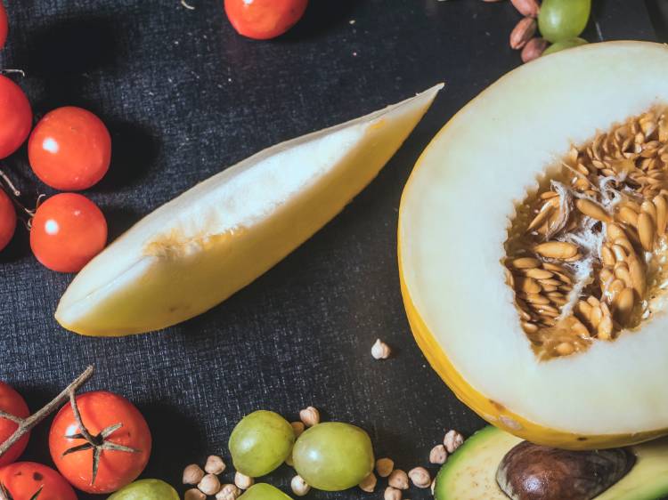 Un melón cortado al medio con otras frutas y vegetales al rededor