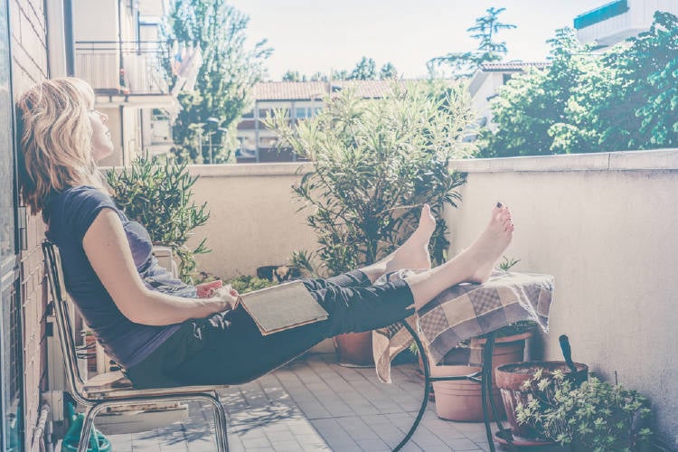 Mujer sentada en un balcón con plantas y un libro sobre sus piernas