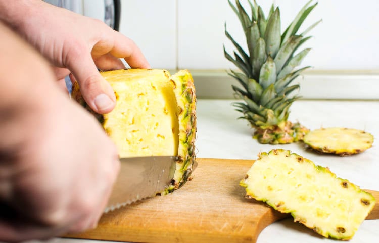 persona cortando la piel de la piña sobre una tabla de madera