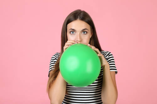mujer infla un globo verde con su boca