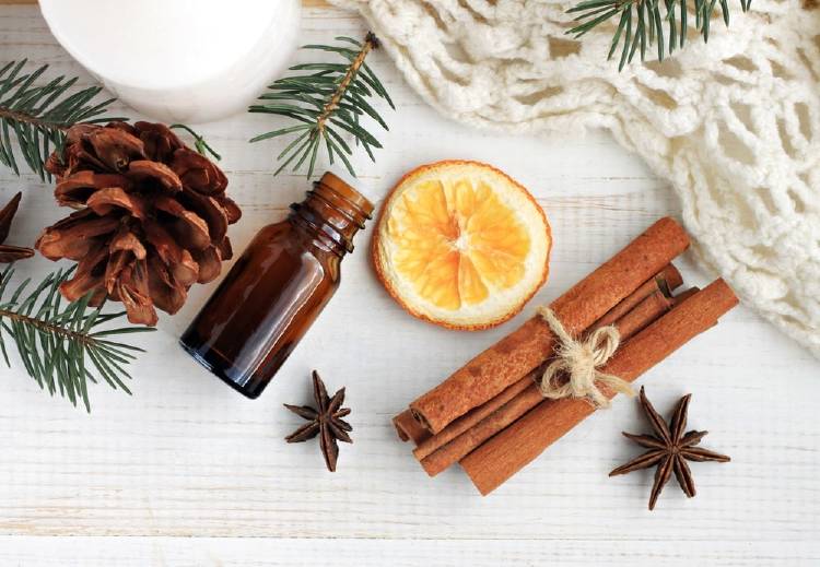 star anise, pine branches, cinnamon sticks tied, orange cut in half, empty extract container and woven tablecloth next to a white candle