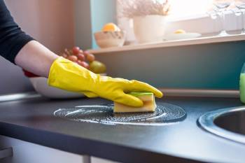 persona limpia su cocina con una esponja y un guante amarillo