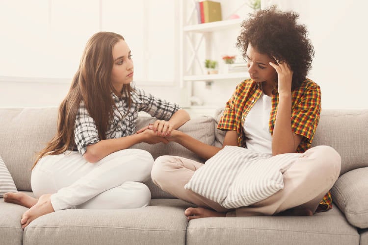 Dos mujeres conversando en un sillón, una consuela a la otra