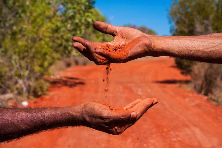 tierra manos Una mano deja caer tierra roja sobre otra