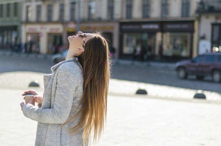 mujer con cabello liso en plaza con café en la mano