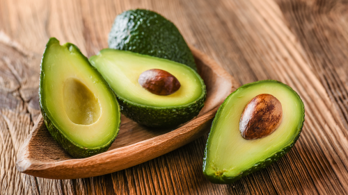 Aguate picado por la mitad con semilla y sin semilla dentro de un plato de madera sobre una mesa de madera Aguate picado por la mitad con semilla y sin semilla dentro de un plato de madera sobre una mesa de madera