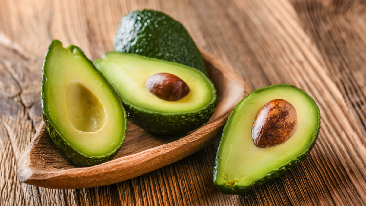 Avocado chopped in half with seed and seedless inside a wooden plate on a wooden table