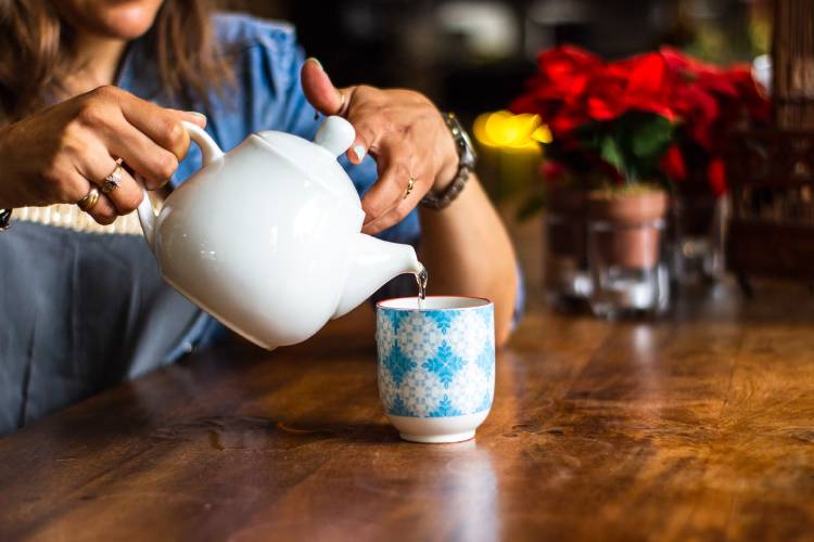 mujer sirviendose una taza de té sentada en una mesa de madera