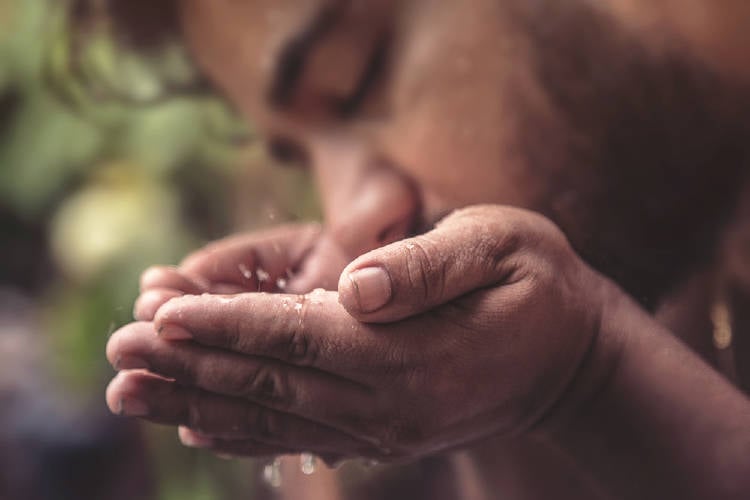 Un hombre bebe agua de sus manos