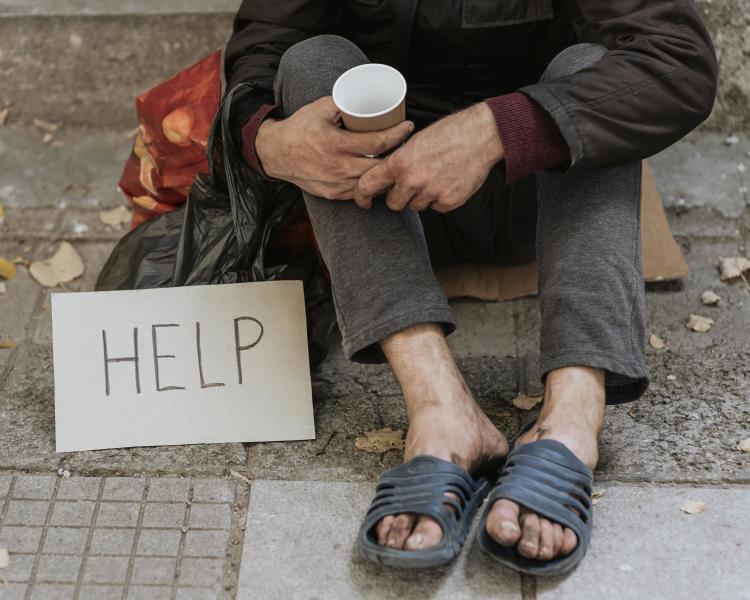 front view of homeless man outdoors with help sign and cup