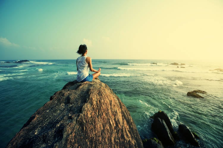 Mujer meditando frente al océano.