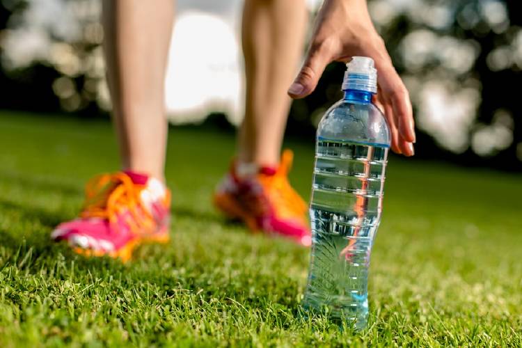 mujer recoge botella de agua luego de hacer ejercicio