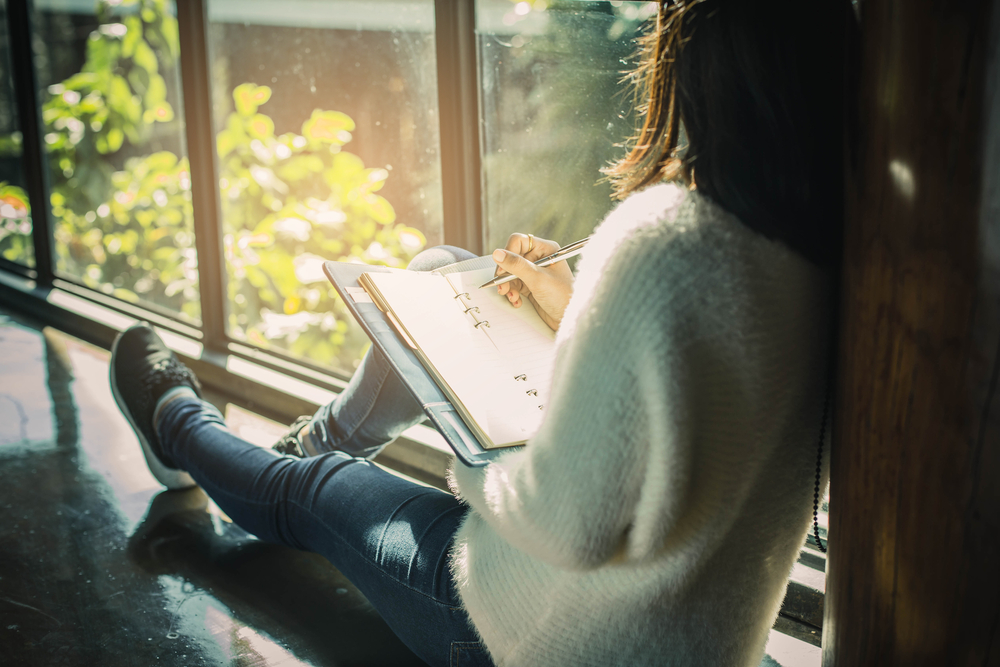 mujer escribe en su cuaderno mirando hacia la ventana
