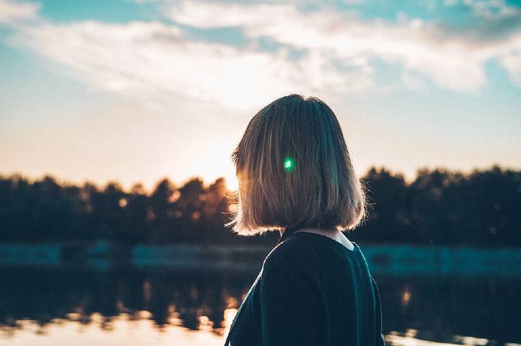 Una mujer de espaldas frente a un lago con árboles de fondo