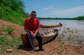 Aborigen boliviano sobre canoa al borde del río Berni contaminado