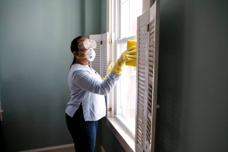 senora limpiando ventanas con guantes, tapabocaa y lente