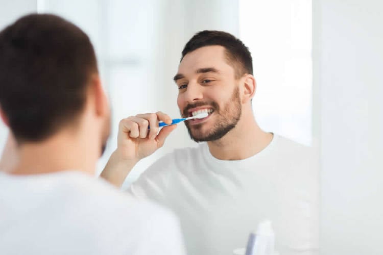 hombre cepilla sus dientes frente al espejo con remera blanca