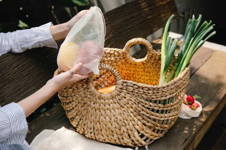 Persona sosteniendo una bolsa reutilizable con frutas junto a una canasta con vegetales