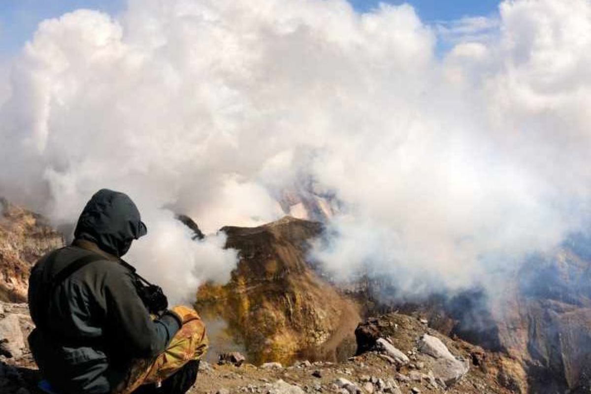 A person sitting on a mountain top watching plumes of smoke from a volcano waking up. (Representative Cover Image Source: Getty Images | Yevgen Timashov) greenmatters.com