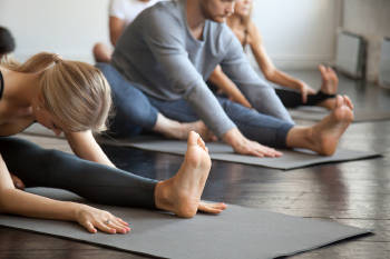alumnos en clase de yoga estiran sus piernas y bajan sus pechos