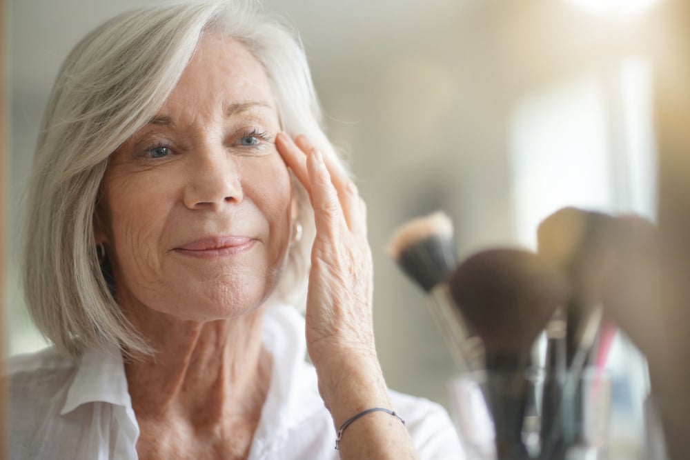 Una mujer con canas se maquilla frente al espejo