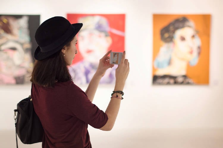 joven observa obras de arte y las captura con su movil en un museo de arte moderno