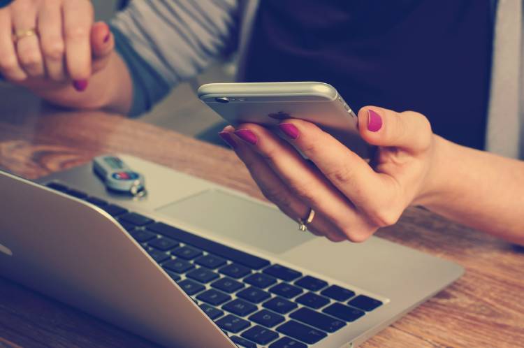 Una mujer usando su celular frente a su computadora