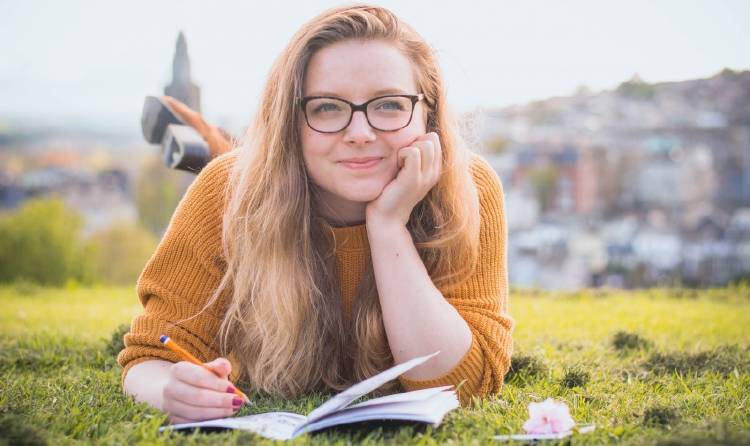 Una mujer escribe en un cuaderno recostada sobre el césped