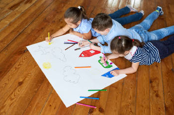 tres niños pequeños dibujan con colores sobre el un papel blanco en el suelo
