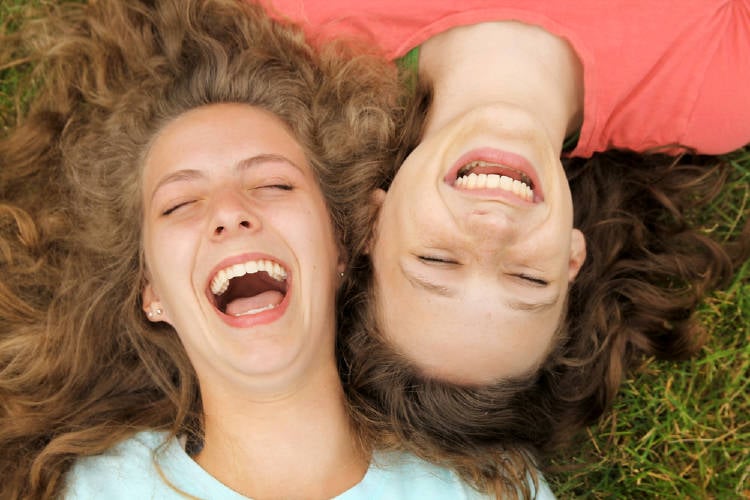 dos amigas se ríen a carcajadas sobre el pasto