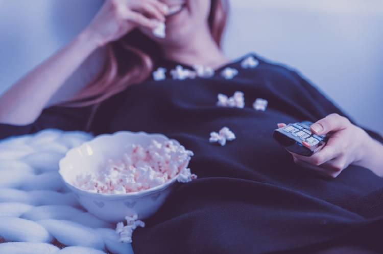 Una mujer mira televisión en la cama y come palomitas