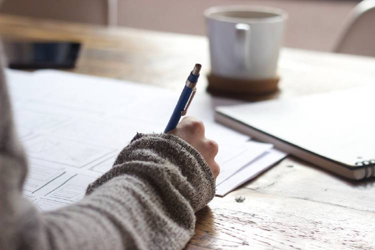 Una persona escribiendo en un escritorio con una taza de café