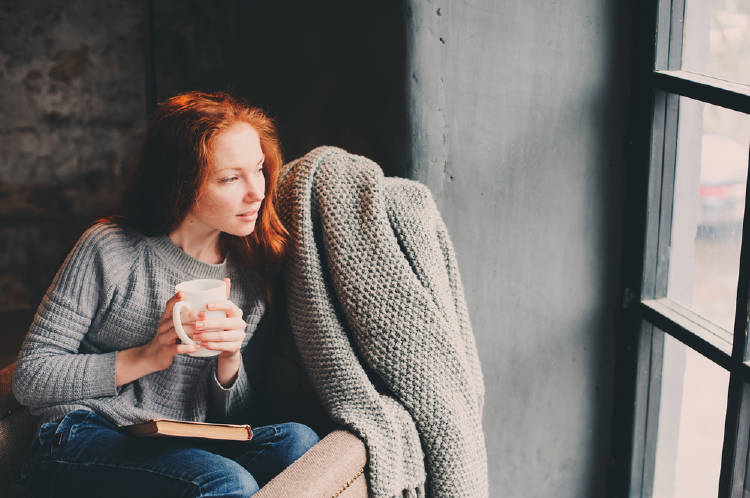 mujer pelirroja disfruta de un libro y un cafe en su hogar hygge