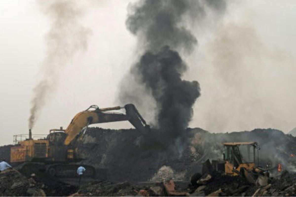Una columna de humo se eleva mientras un trabajador maneja una excavadora para transportar montones de carbón en bruto en las afueras de Dhanbad, en el estado indio de Jharkhand© Vishal kumar singh