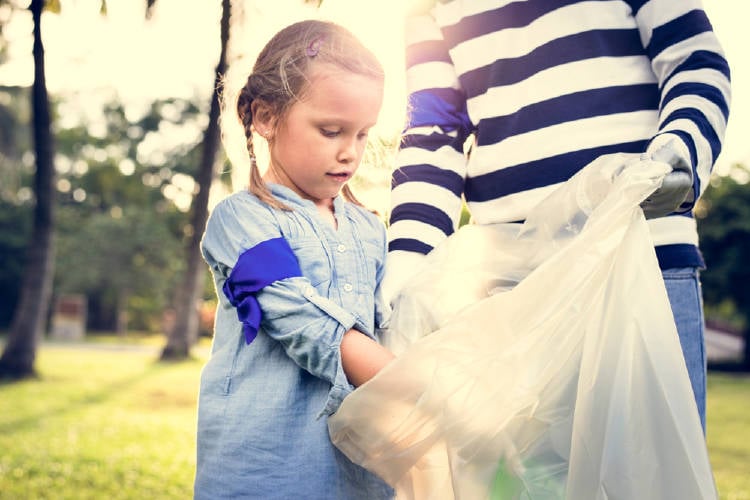 Una niña arrojando residuos en una bolsa en un parque