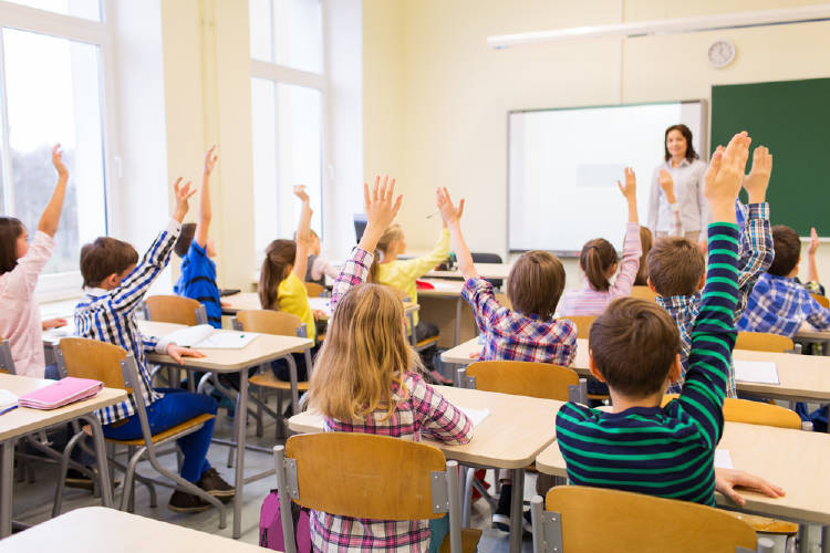 Niños participan en una clase levantando la mano.