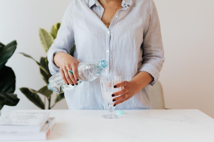 Mujer sirviendo agua de una botella de plástico en un vaso