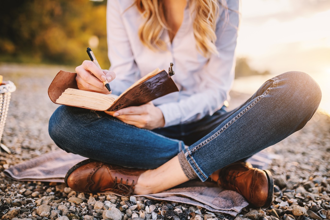 Mujer escribiendo en un cuaderno sentada al aire libre Mujer escribiendo en un cuaderno sentada al aire libre