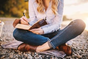 Mujer escribiendo en un cuaderno sentada al aire libre