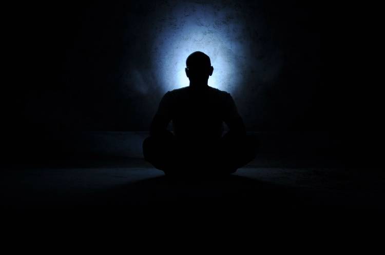 Una persona meditando en la oscuridad con una luz que irradia de su cabeza
