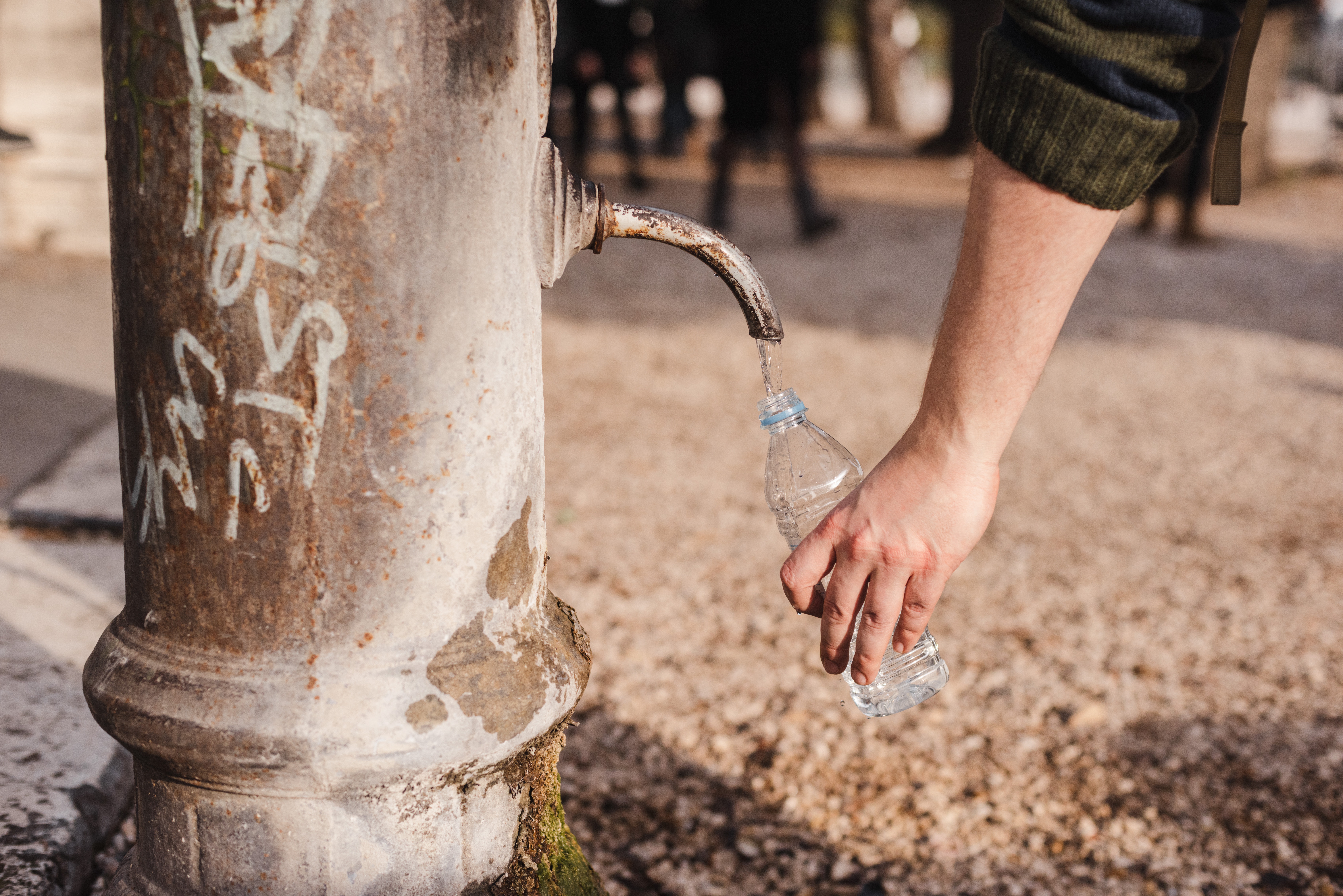 Foto de Olga Lioncat en Pexels Persona llenando una botella de agua en el parque