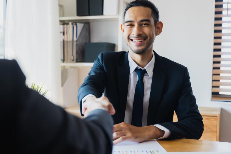 Hombre de traje azul sonriendo y estrechando la mano de una persona en una entrevista de trabajo