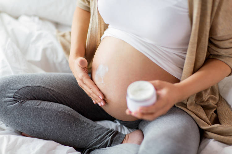 Una embarazada se pone crema en la panza