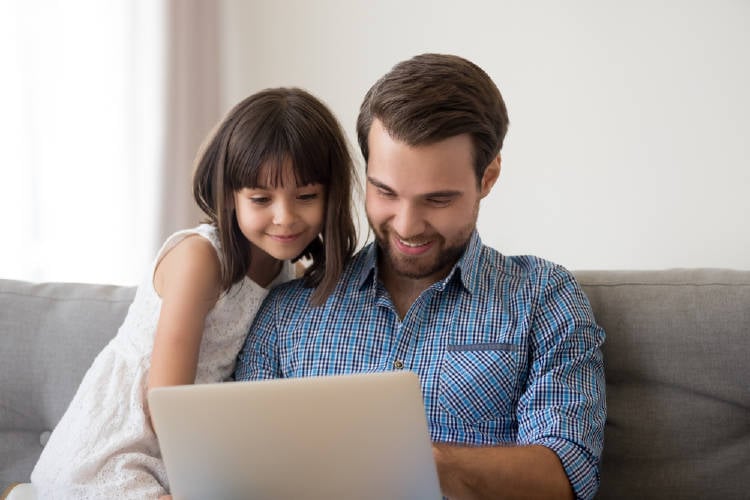 padre e hija sonrientes miran la pantalla de la computadora 